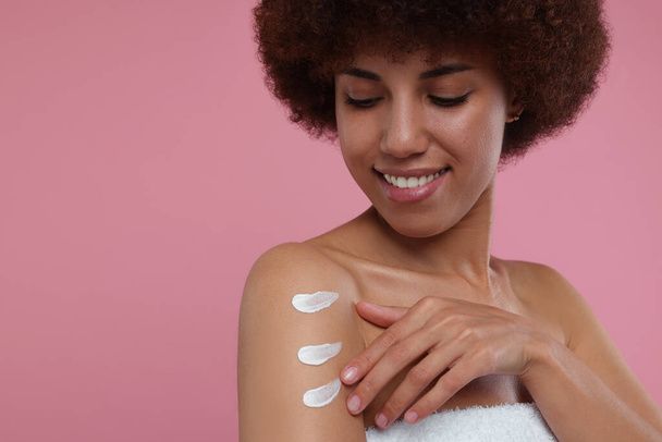 Beautiful young woman applying body cream onto arm on pink background, space for text - 写真・画像