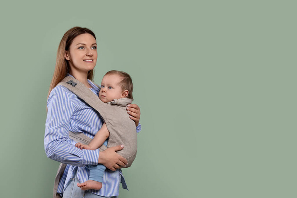 Mother holding her child in sling (baby carrier) on olive background. Space for text - Foto, imagen