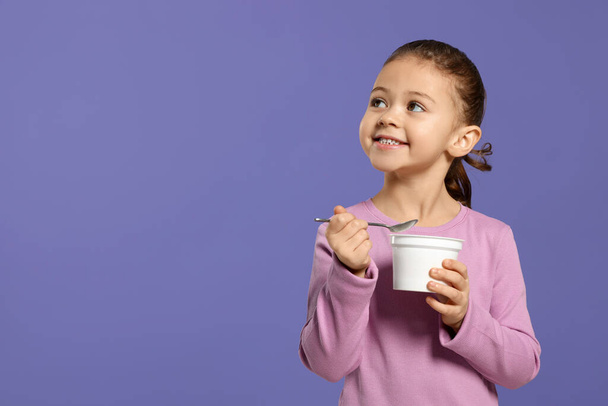 Girl with tasty yogurt on violet background, space for text - Fotoğraf, Görsel