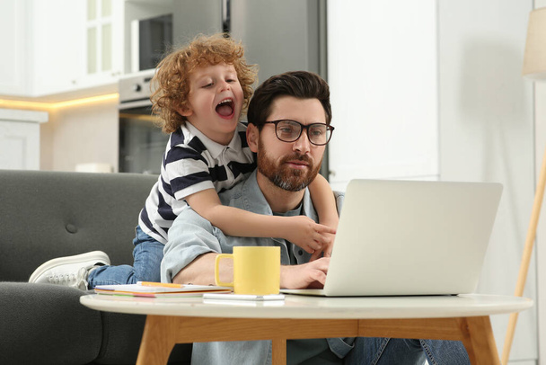 Egy férfi laptoppal, aki távolról dolgozik otthon. Apa és fia az asztalnál. - Fotó, kép