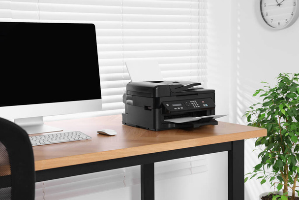 Impresora moderna con papel cerca de la computadora en la mesa de madera en casa oficina - Foto, imagen
