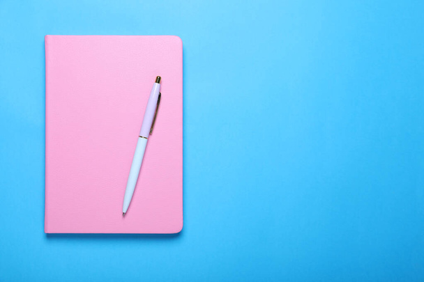 Closed pink notebook and pen on light blue background, top view. Space for text - Foto, Bild