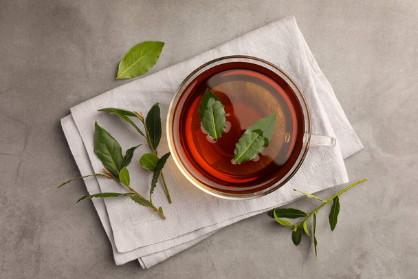 Cup of freshly brewed tea with bay leaves on grey table, flat lay - Photo, image