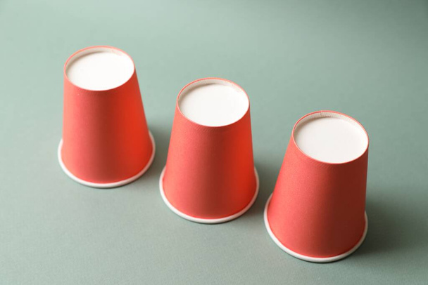 Three red cups on pale olive background. Thimblerig game - Fotoğraf, Görsel