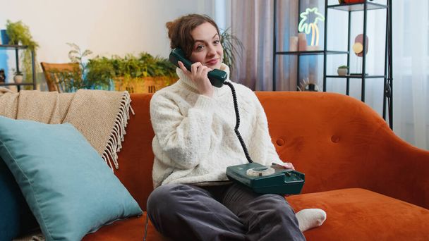 Muotokuva nuori nainen tekee langallinen puhelinkeskustelu ystävien kanssa istuu puhelun sohvalla kotona huoneessa. Iloinen innoissaan kaunis tyttö nauttia vanhanaikainen retro puhelin 90 puhua sisällä - Valokuva, kuva