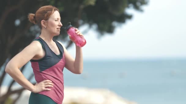 Mulher esportiva adulta sem maquiagem bebe água da garrafa de plástico ao ar livre. A meio do tiro - Filmagem, Vídeo