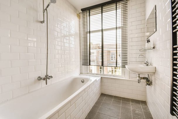 Yerde siyah beyaz fayanslar, küvet, duş ve arka planda pencere olan beyaz bir banyo. - Fotoğraf, Görsel