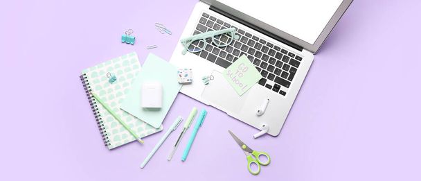 Sticky note with text GO TO SCHOOL, different stationery, laptop and earphones on lilac background - Φωτογραφία, εικόνα