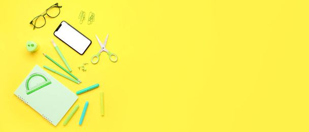 Cellulare con occhiali e diversi articoli di cancelleria su sfondo giallo. Banner per il design - Foto, immagini