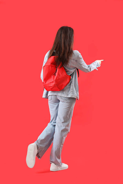 バックパックを持っている女性学生は、赤い背景に何かを指して、バックパックビュー - 写真・画像