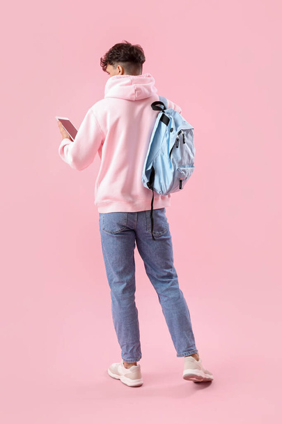 Male student with tablet computer and backpack on pink background, back view - Valokuva, kuva
