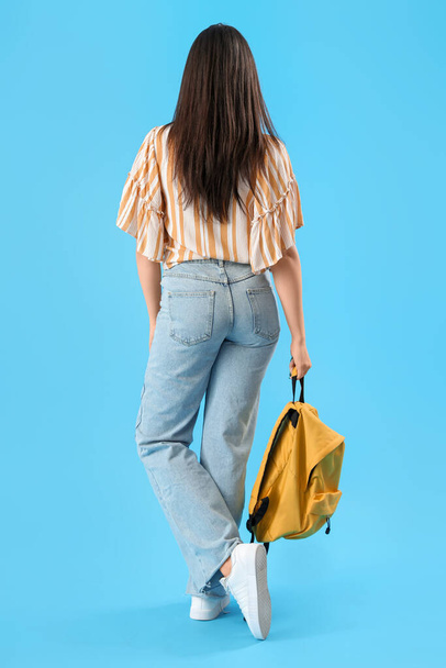 Female student with backpack on blue background, back view - Valokuva, kuva