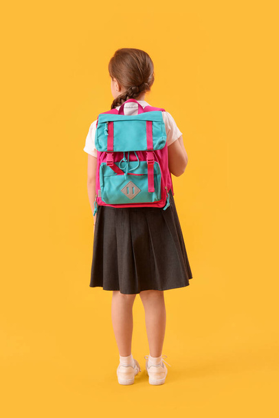 Little schoolgirl with backpack on yellow background, back view - Foto, Imagem