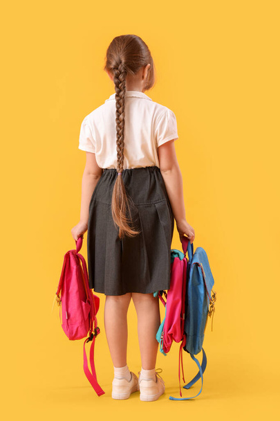 Little schoolgirl with backpacks on yellow background, back view - Foto, immagini