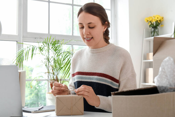 Young woman packing parcel for client in office - Foto, Bild