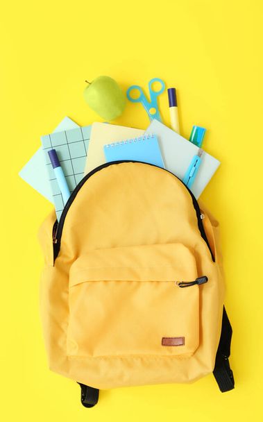 Σακίδιο πλάτης σχολείο χρώμα με μήλο, σημειωματάρια και δείκτες σε κίτρινο φόντο - Φωτογραφία, εικόνα