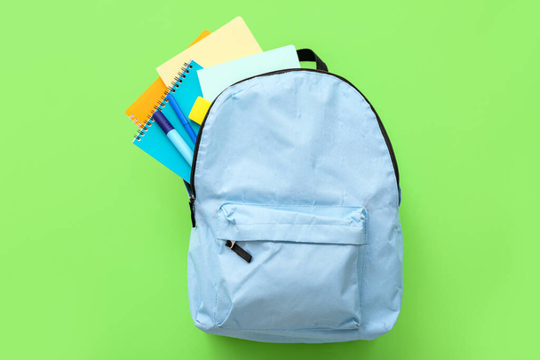 Blauwe schoolrugzak met notitieboekjes en markeringen op groene achtergrond - Foto, afbeelding