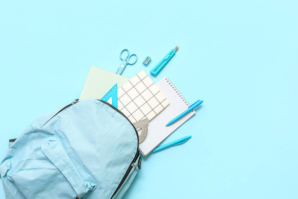 Mochila escolar con diferentes artículos de papelería sobre fondo azul - Foto, Imagen