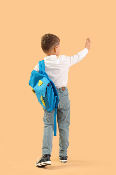 Little schoolboy with backpack waving hand on orange background, back view - Foto, Imagem