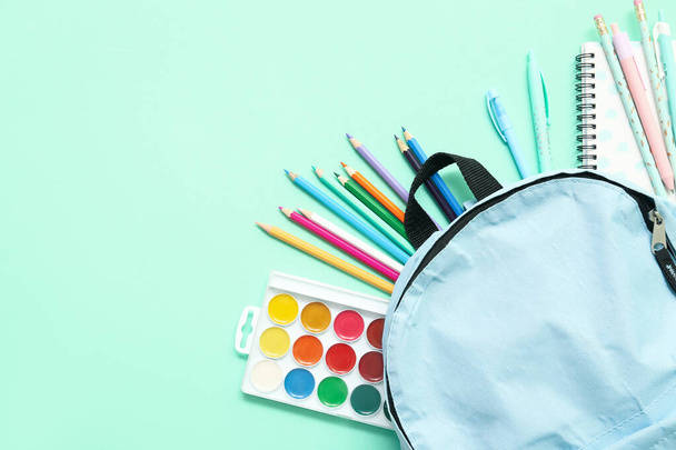 Mochila escolar con diferentes lápices y pinturas de colores sobre fondo turquesa - Foto, imagen