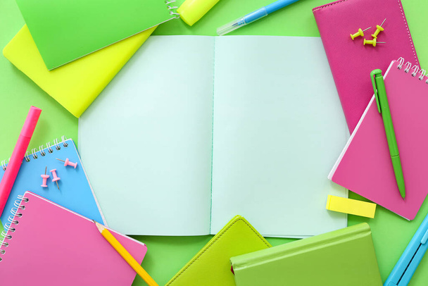 Papel en blanco con diferentes cuadernos de colores sobre fondo verde - Foto, imagen