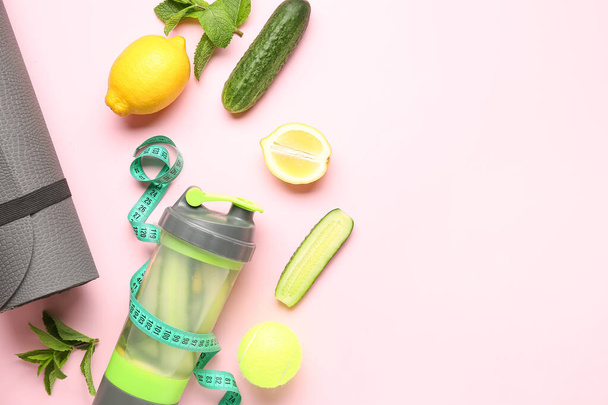 Bottle of lemonade with cucumber and sport equipment on pink background - Photo, Image