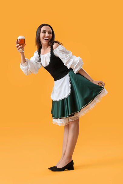 Hermosa camarera Octoberfest con cerveza bailando sobre fondo amarillo - Foto, Imagen