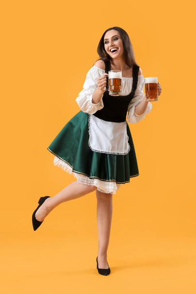 Beautiful Octoberfest waitress with beer dancing on yellow background - Photo, Image
