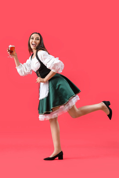 Beautiful Octoberfest waitress with beer dancing on red background - Photo, Image