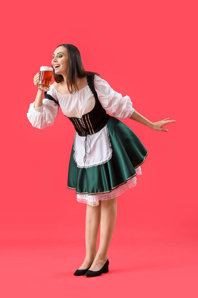 Beautiful Octoberfest waitress with beer dancing on red background - Foto, Bild