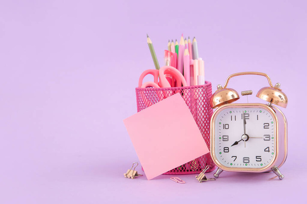 Alarm clock with different stationery on lilac background - Foto, imagen