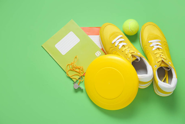 Sneakers with frisbee, tennis ball, whistle and notebooks on green background - Photo, image