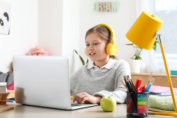 Kleines Mädchen mit Kopfhörer und Laptop beim Unterricht zu Hause - Foto, Bild