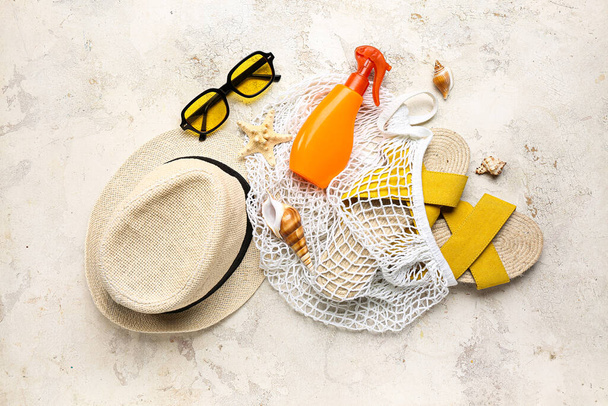 Sac à ficelle avec lunettes de soleil, bouteille de crème solaire et accessoires de plage sur fond clair grunge - Photo, image