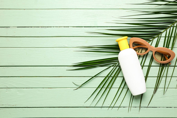 Sunglasses with bottle of sunscreen cream and palm leaf on green wooden background - Foto, Bild