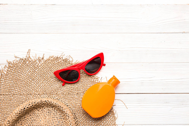 Chapeau en osier avec lunettes de soleil et bouteille de crème solaire sur fond blanc en bois - Photo, image