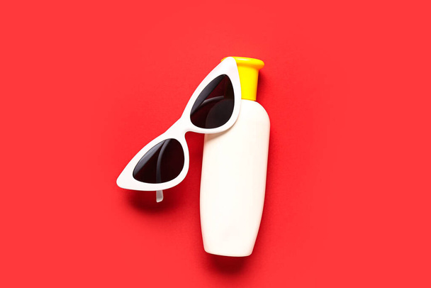 Gafas de sol con botella de crema protector solar sobre fondo rojo - Foto, imagen