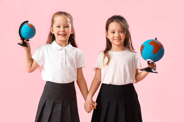 Little schoolgirls with globes on pink background - Foto, imagen