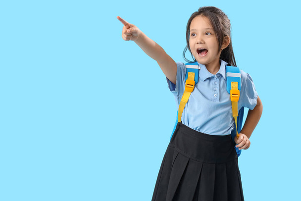 Kis iskoláslány hátizsákkal mutat valamit világoskék háttér - Fotó, kép