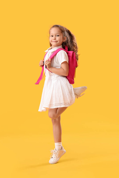 Jumping little schoolgirl on yellow background - 写真・画像