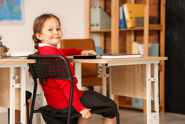 Little schoolgirl sitting at desk  in classroom - Foto, afbeelding