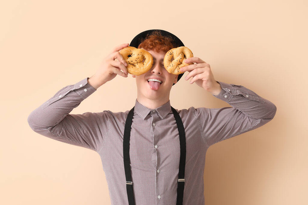 Jovem em roupas tradicionais alemãs com pretzels mostrando língua no fundo bege - Foto, Imagem
