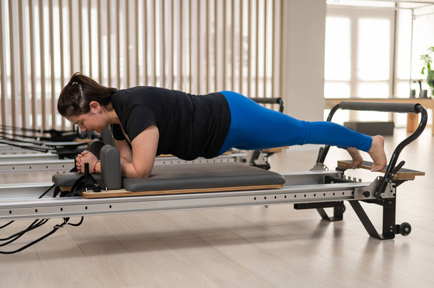 Overweight caucasian woman doing pilates exercises on a reformer - 写真・画像