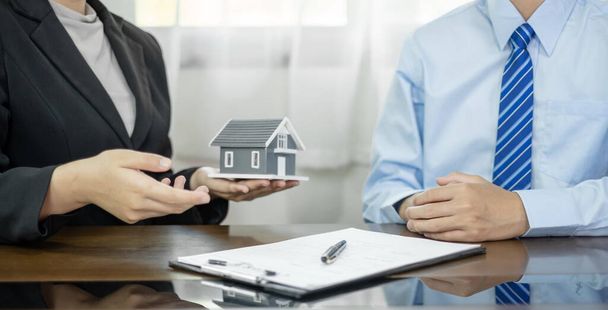 Un agent immobilier avec le modèle de maison parle à des clients au sujet de la souscription d'une assurance habitation. Concept d'assurance habitation
. - Photo, image