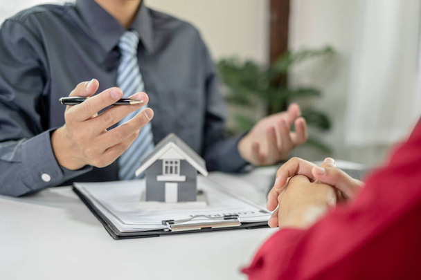 Ein Immobilienmakler mit einem Eigenheimmodell spricht mit Kunden über die Anmietung eines Hauses und den Kauf einer Hausversicherung und schließt den Vertrag nach Abschluss der formellen Verhandlungen ab.. - Foto, Bild