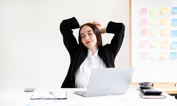 Asyalı kadın muhasebeci, ofiste çalışırken rahatlamak ve dinlenmek için sandalyede çalışmaktan yoruldu.. - Fotoğraf, Görsel