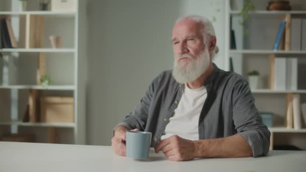 Ernsthafter alter Mann sitzt am Tisch und bei einer Tasse Kaffee. Entspannter älterer Mann mit einer Tasse Tee, der über sein Leben nachdenkt. Kaffee für Senioren. Tee für Senioren. - Filmmaterial, Video