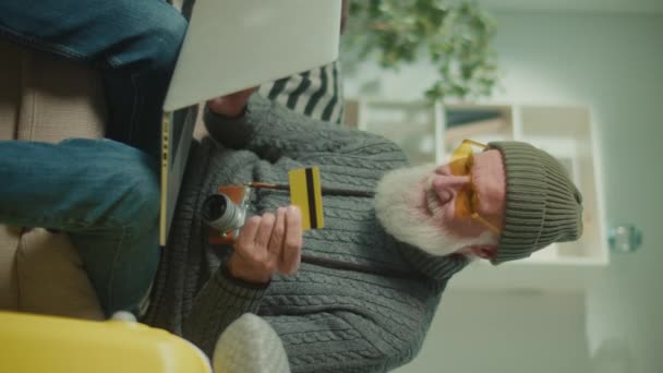Vertikale Ansicht. Porträt eines alten Mannes Reisenden mit Kreditkarte. Ein älterer Mann Verbraucher mit Hut und lustigen Brillen, die für einen Einkauf in einem Web-Store.E-Commerce. - Filmmaterial, Video