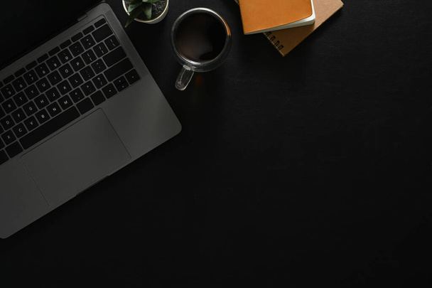 現代の職場、ノートパソコン付きのブラックオフィスデスク、コーヒーとノートブックのカップ。コピースペース付きのトップビュー. - 写真・画像