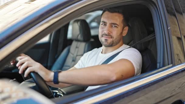 Jonge Spaanse man glimlacht vol vertrouwen zittend op de auto op straat - Video